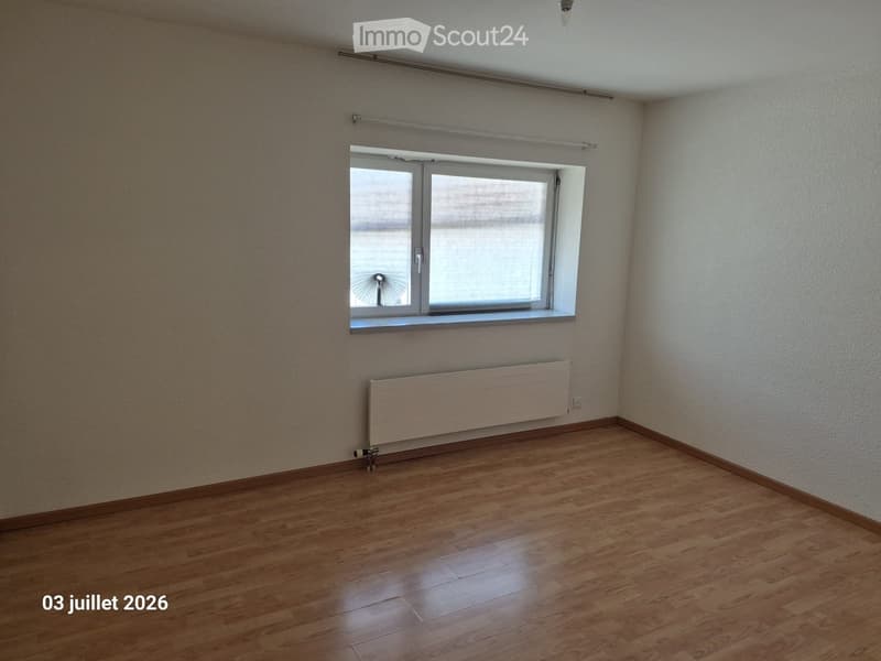 Empty room with wooden flooring, white walls, a single window with blinds, and a radiator below the window.