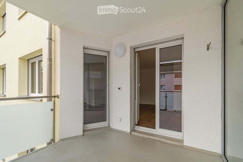 Empty balcony with white walls, large sliding glass doors, and a view of the adjacent building.