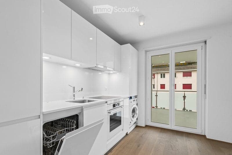 Modern, minimalist kitchen with white cabinets, stainless steel appliances, and a large sliding glass door leading to a balcony.