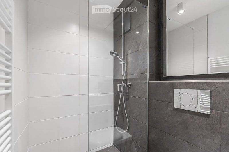 Modern bathroom with white tiled walls, a glass-enclosed shower, a large mirror, and a towel rack.