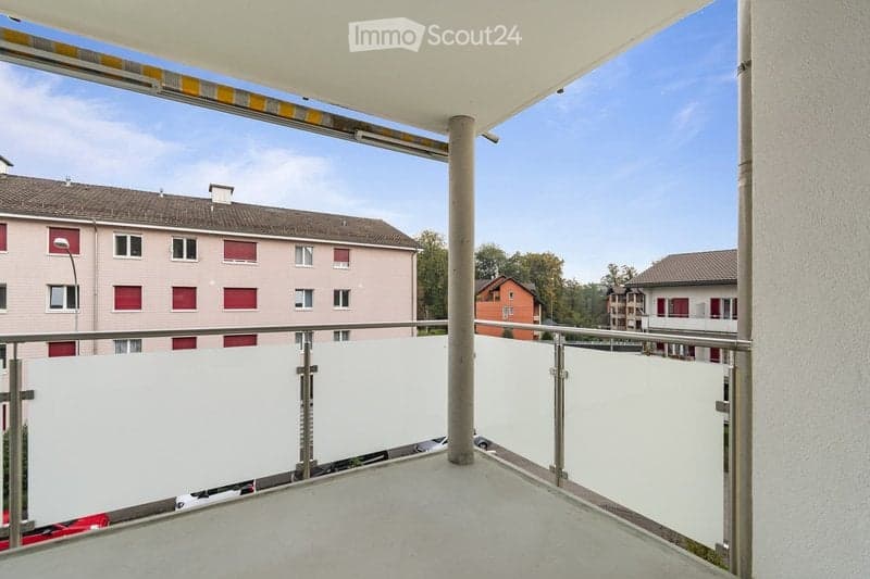 Balcony with metal railing, white privacy screens, and a view of neighboring buildings and trees.