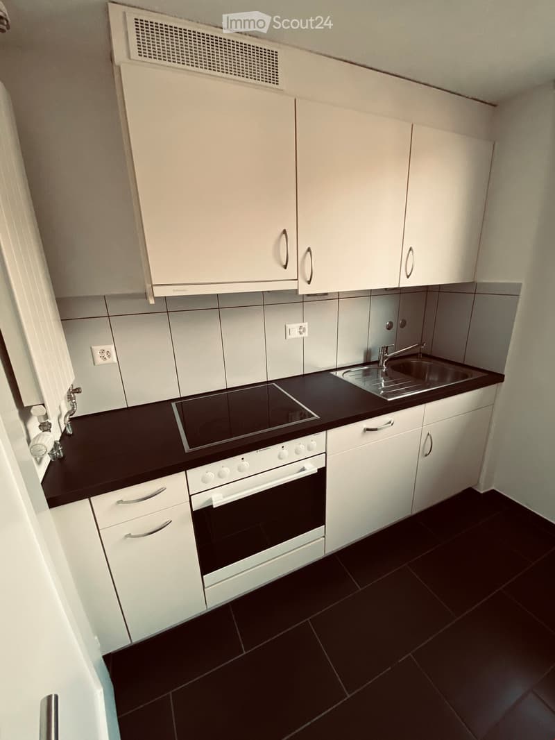 Modern kitchen with white cabinets, black countertops, and black tiled floor. Features an induction cooktop, oven, and sink with a faucet.