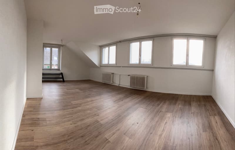 Empty room with wooden flooring, white walls, multiple windows, and radiators along one wall. No furniture or equipment present.