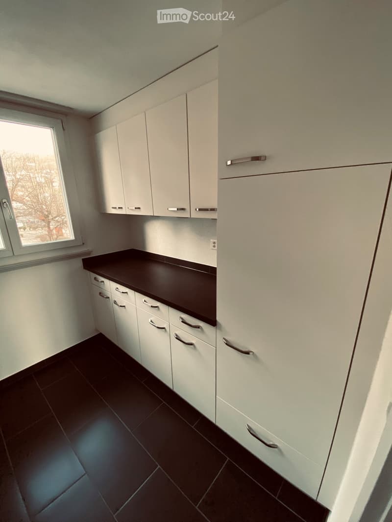 Modern kitchen with white cabinets, dark countertop, and dark tiled floor. Features a window with a view of the outside.