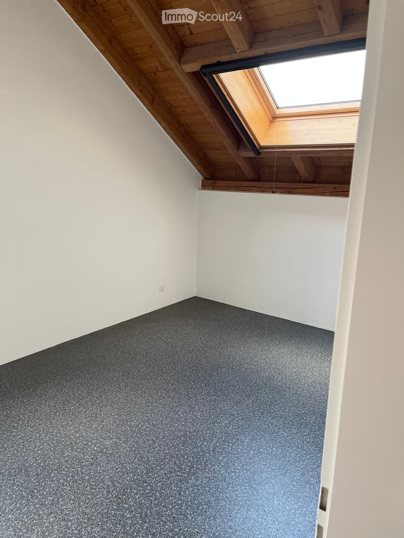 Empty room with grey carpeted floor, white walls, wooden slanted ceiling, and a skylight window.