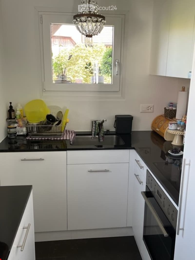 clean and modern kitchen with black countertops, white cabinets, central island, sink, dishwasher, and oven