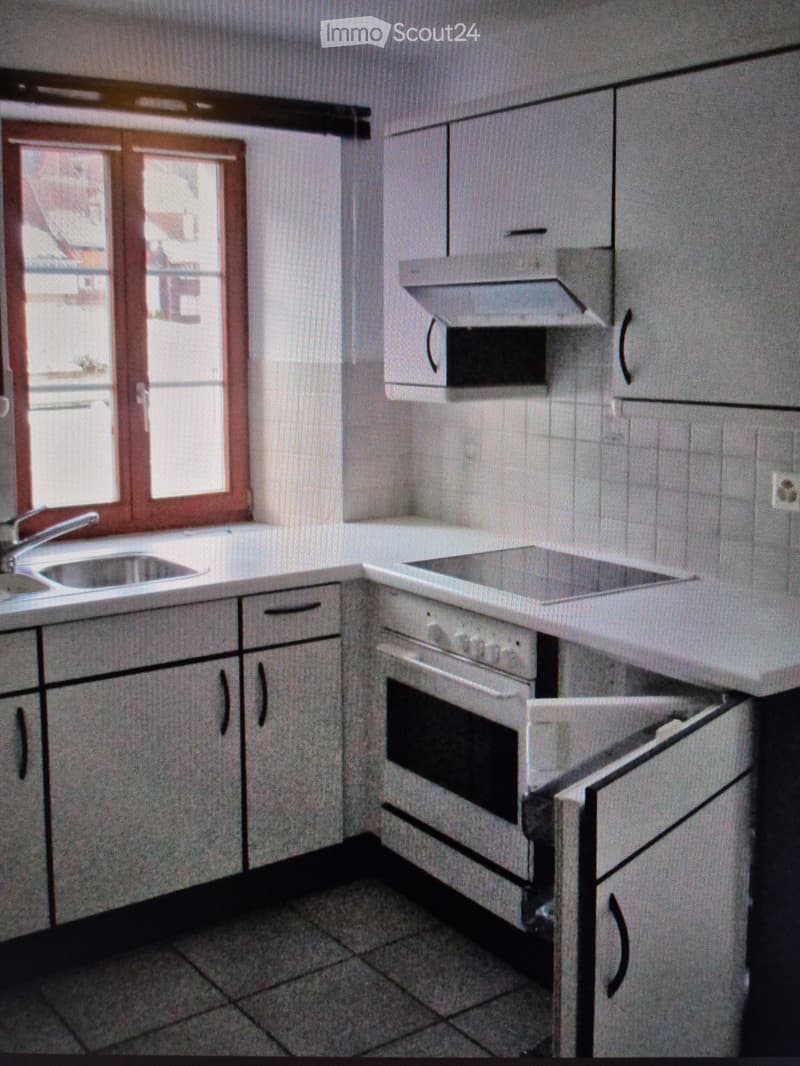 Modern kitchen with white cabinets, a sink, and an oven. The space is well-lit with natural light from a window.