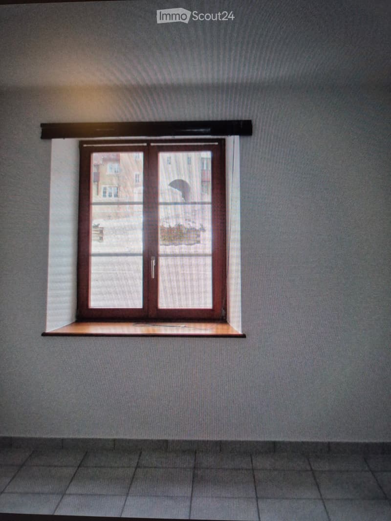 Empty room with grey walls, tiled floor, and a window with a wooden frame and a small wooden sill.