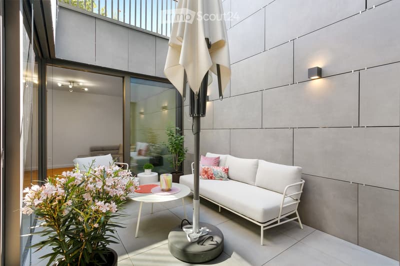 Modern balcony with white sofa, small table, umbrella, and decorative plants.