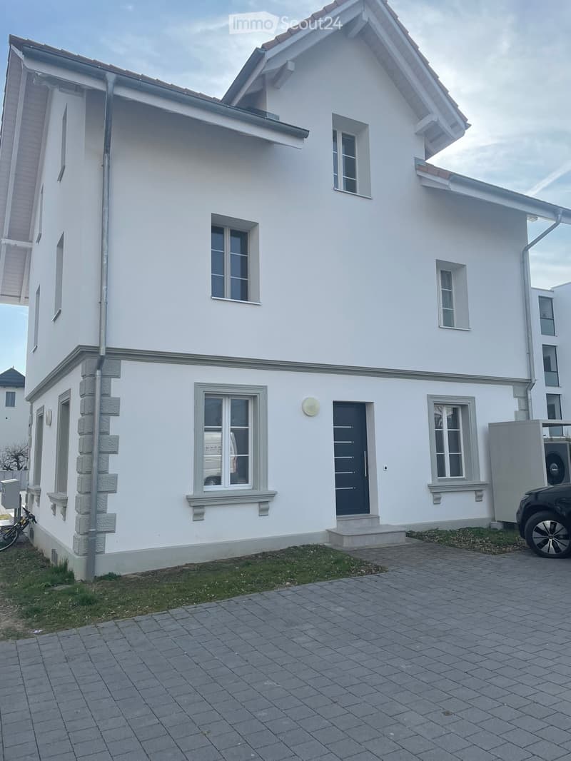 Two-story white house with multiple windows, grey front door, and a paved driveway.