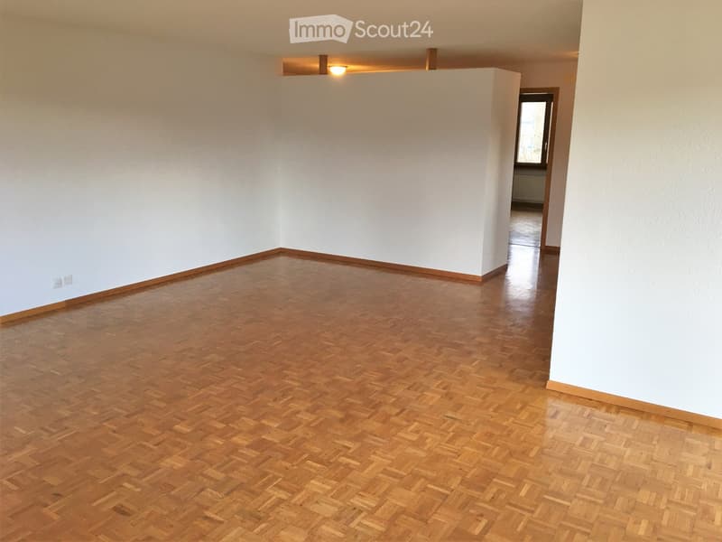 Empty room with wooden parquet flooring and white walls, featuring a recessed ceiling light and a doorway leading to another room.