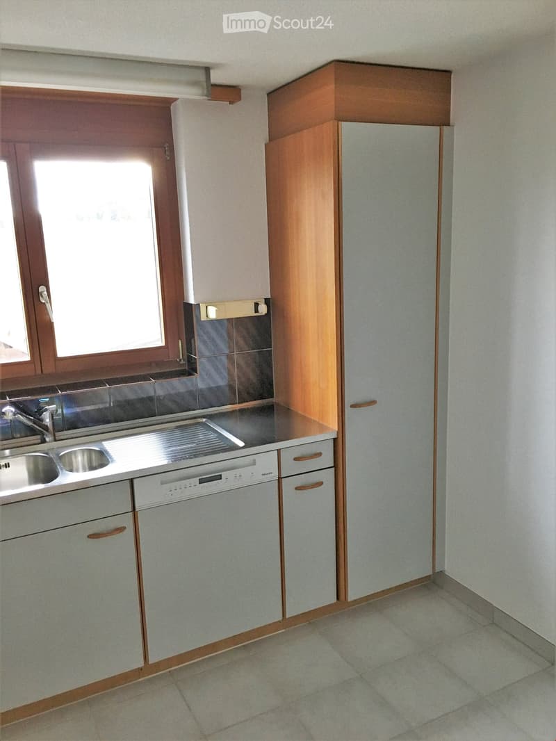 Modern kitchen with light-colored cabinets, stainless steel sink, and dishwasher. Features a window with wooden frame and tiled backsplash.