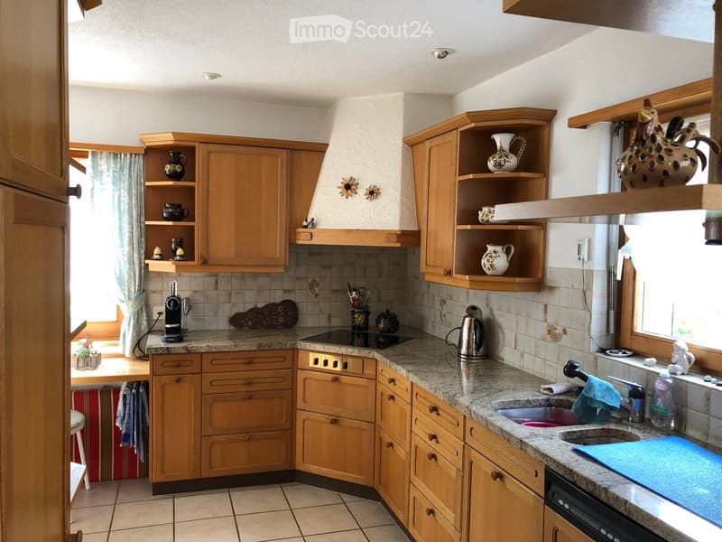 The kitchen features wooden cabinets, granite countertops, and a stainless steel sink with a faucet. A coffee maker and electric kettle are on the counter, along with decorative vases on the shelves.