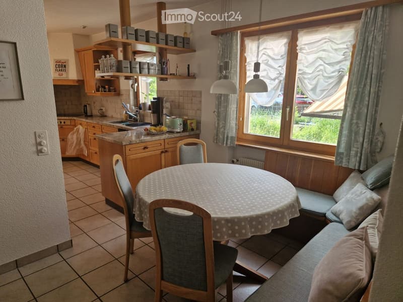 A cozy kitchen and dining area with wooden cabinets, a round dining table with chairs, a built-in sofa, and various kitchen appliances.