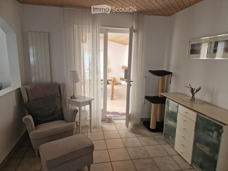 Cozy living room with a grey sofa, ottoman, small side table with lamp, cat tree, and a cabinet with glass doors.