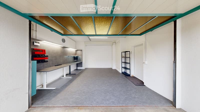 Modern, minimalist room with white walls, grey floor, and a raised ceiling with green and gold panels. Features include a long bench, a small table, and a black shelving unit.