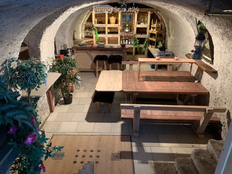 An outdoor seating area with wooden tables, benches, and bar counter, featuring stone walls and a rustic ambiance.