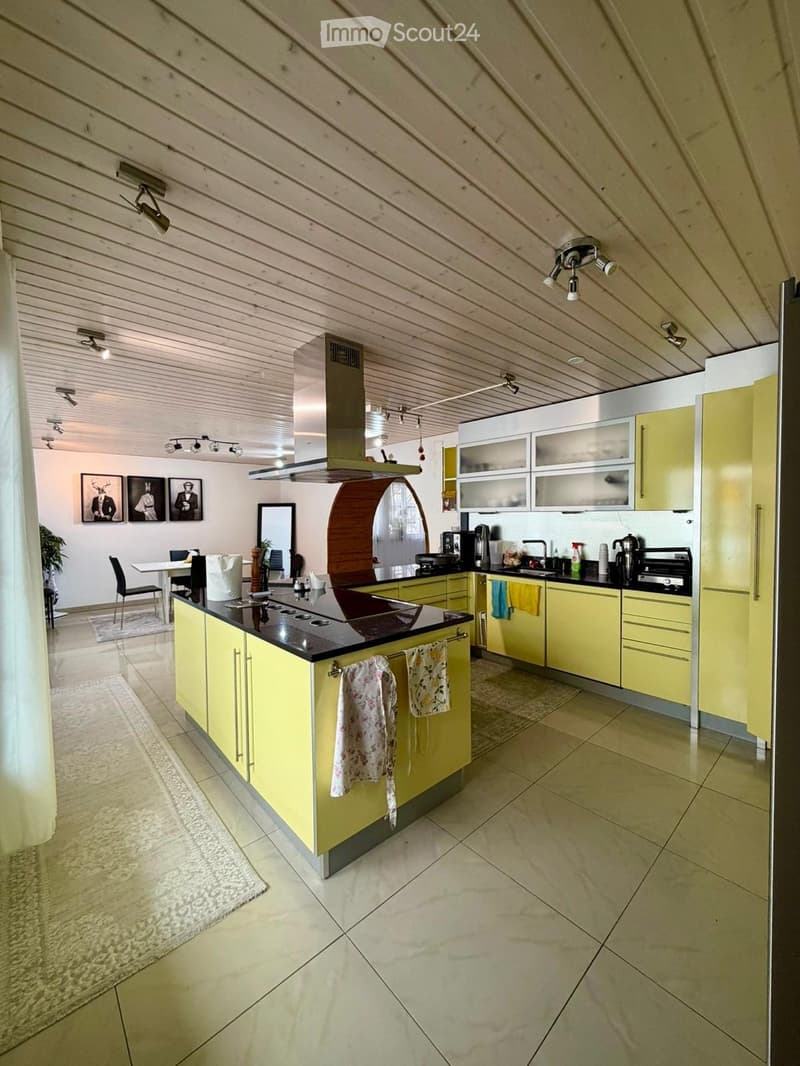 Bright kitchen with yellow cabinets, a central island, and modern appliances. Features a dining area with a table and chairs, and a mirror on the wall.