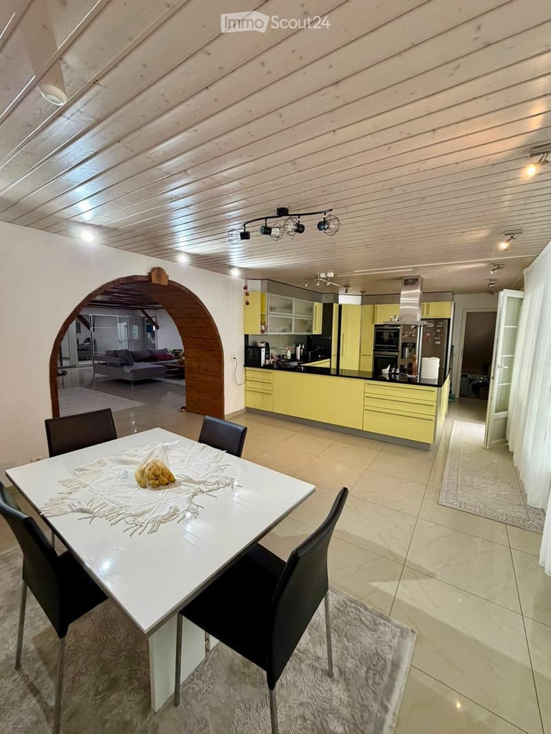Dining area with a white dining table, four black chairs, and a modern kitchen with yellow cabinets, stainless steel appliances, and a black countertop.
