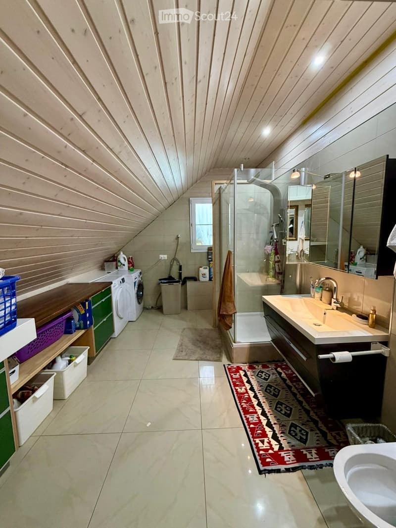 Bathroom with wooden walls and ceiling, featuring a sink with a mirror, a shower, a washing machine, and storage shelves.
