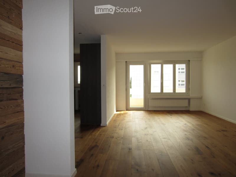 Empty room with wooden flooring, white walls, large windows, and a radiator. No furniture or equipment present.