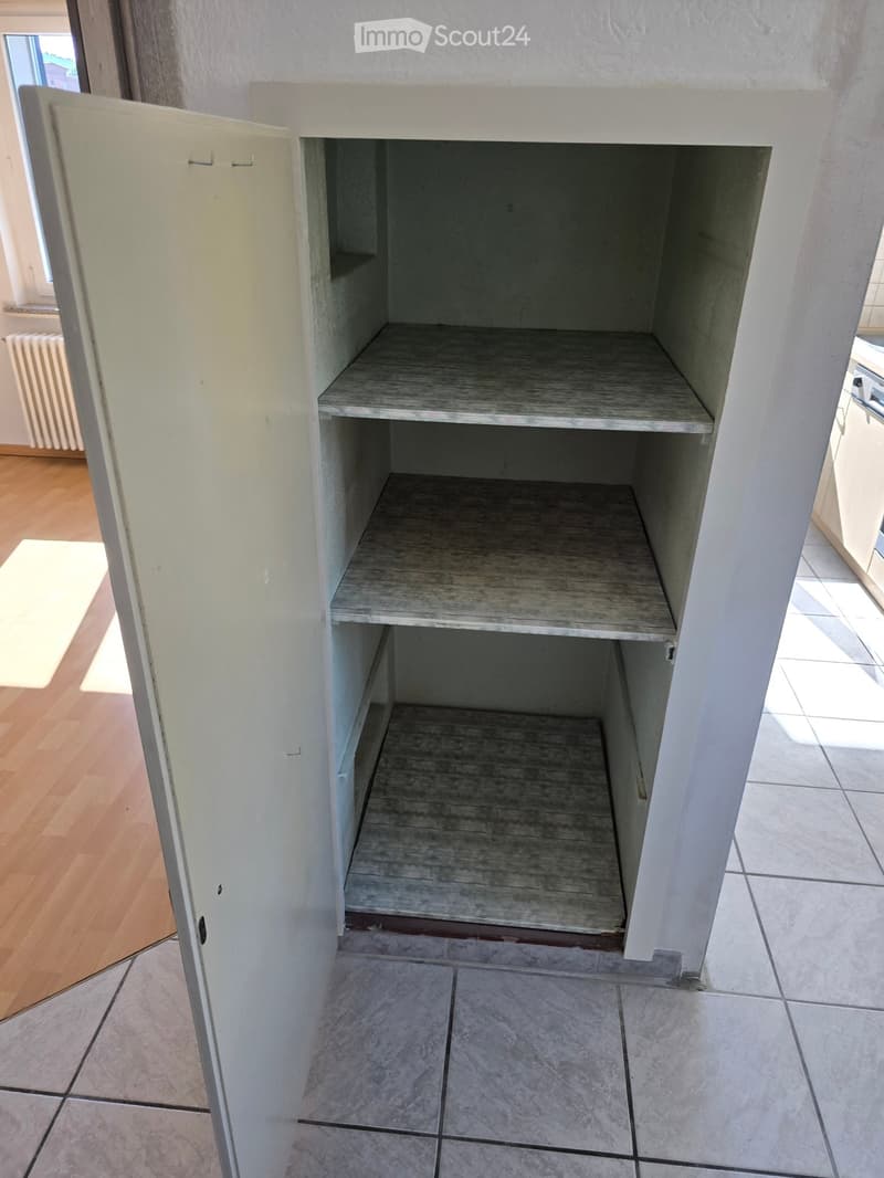 Empty kitchen cabinet with wooden shelves, white frame, and tiled floor. No appliances or items visible.