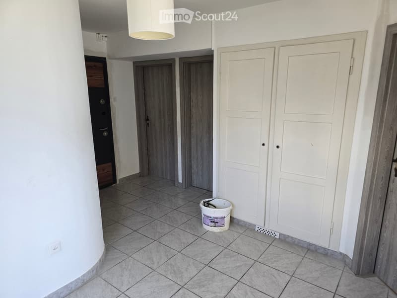 Empty hallway with tiled floor, white walls, several doors, and a white bucket on the floor.