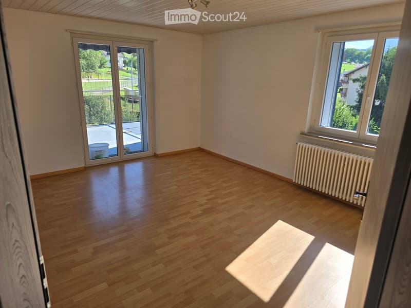 Empty room with wooden flooring, large windows, and a sliding glass door leading to a balcony area.