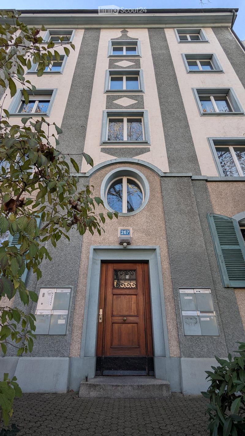 Facade of a multi-story residential building with a wooden front door, decorative windows, and mailboxes.