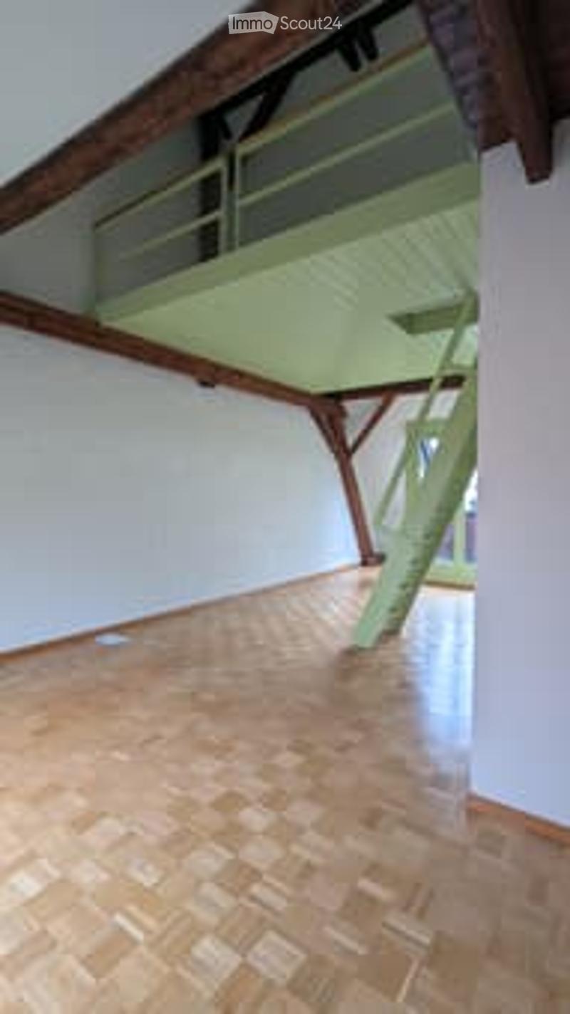 Empty room with wooden floor and exposed wooden beams on the ceiling. A staircase leads to an upper level.