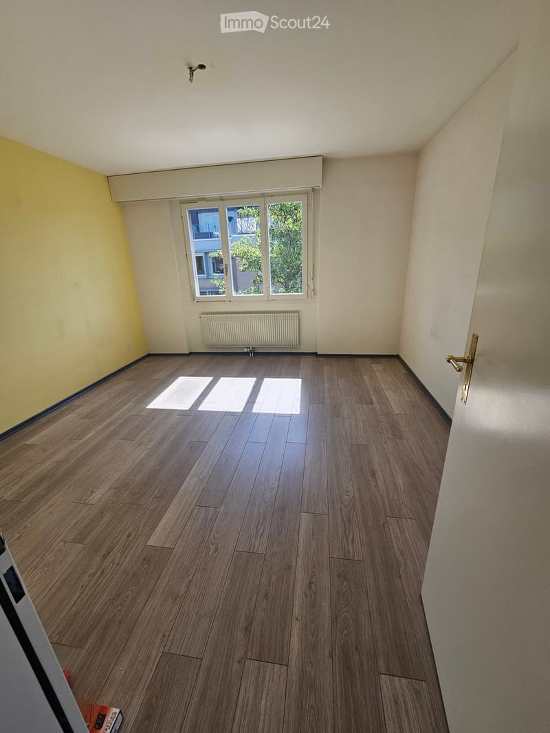 Empty room with wooden flooring, white walls, a window with blinds, and a radiator below it.
