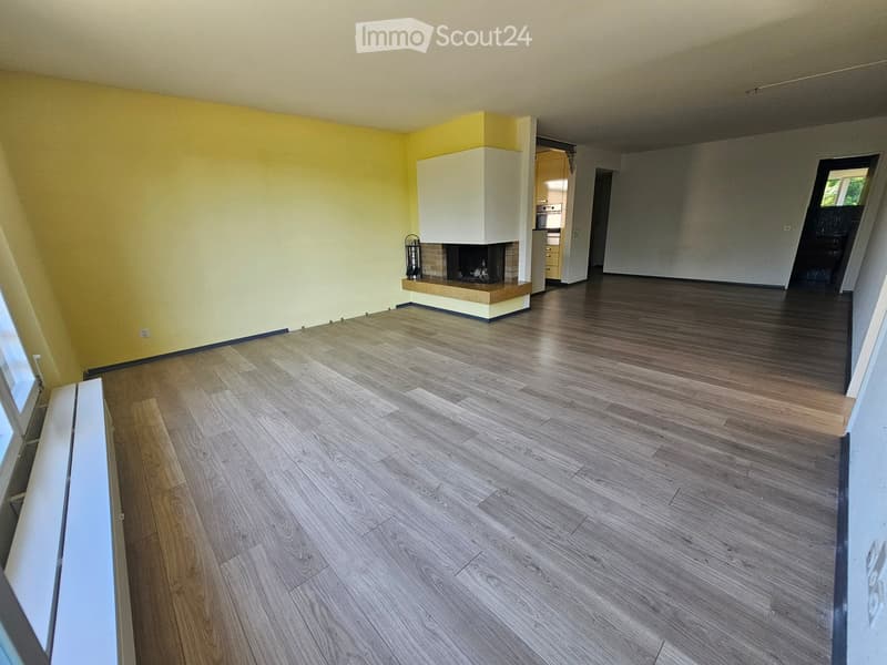 Empty room with wooden flooring, yellow walls, fireplace, and open doorway to another room.