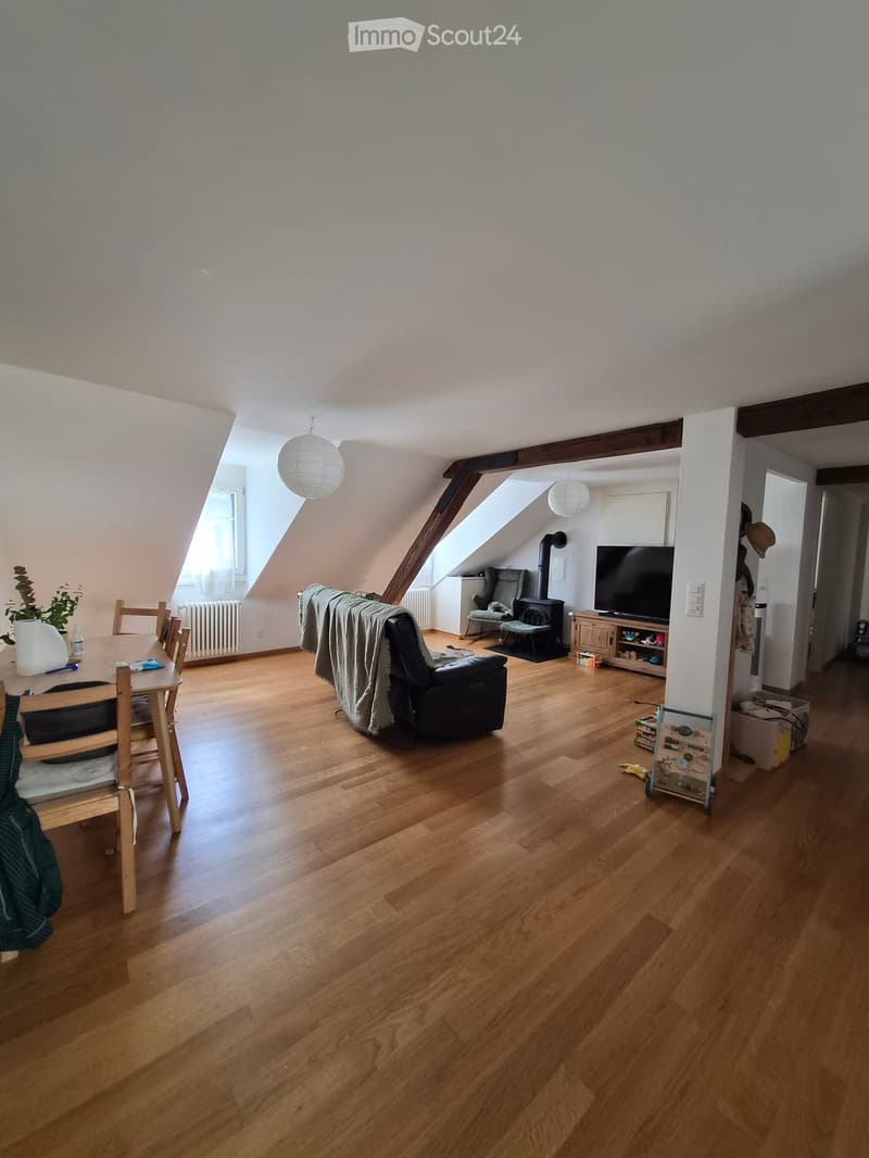 Bright attic living space with wooden flooring, exposed wooden beams, skylights, a sofa, dining table, TV, and fireplace.