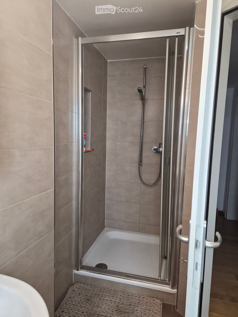 Modern bathroom with a bathtub, glass-enclosed shower, and a small shelf holding toiletries.