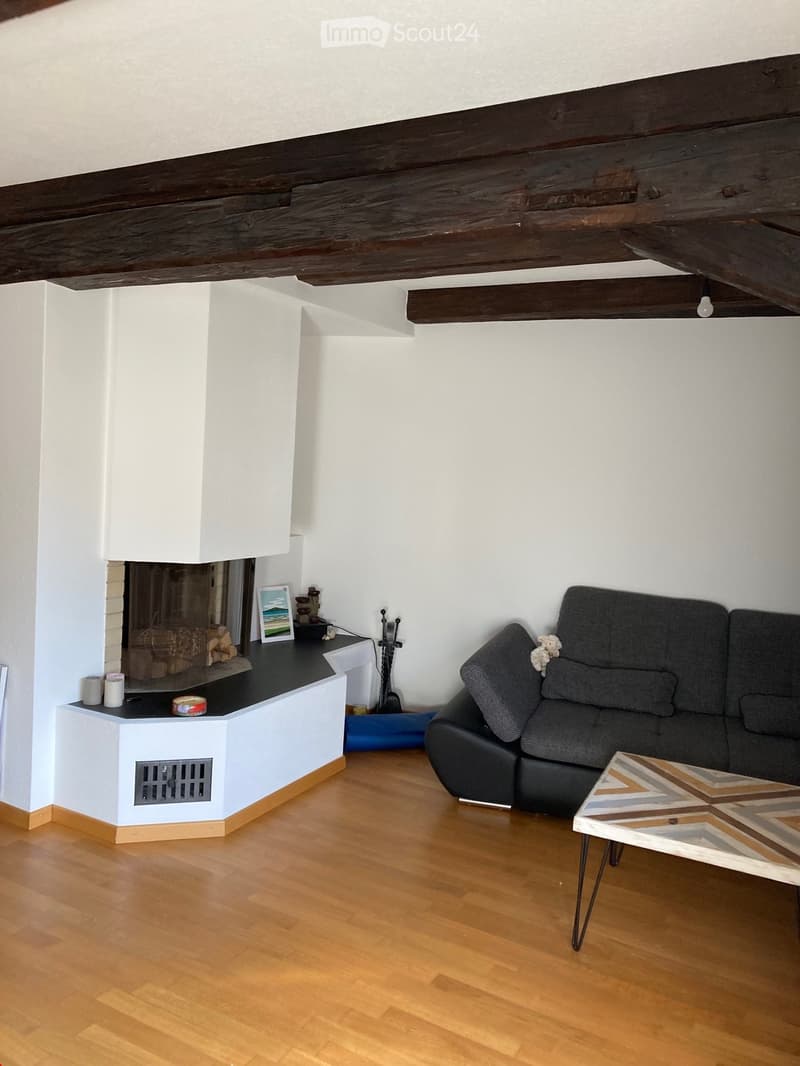 Living room with exposed wooden beams, fireplace, sofa, coffee table, and picture frame on mantel.