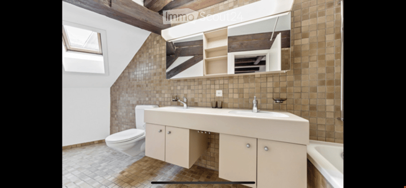 Modern bathroom with a double sink vanity, large mirror, toilet, and bathtub. Exposed wooden beams on the ceiling and brown tiled walls and floor.
