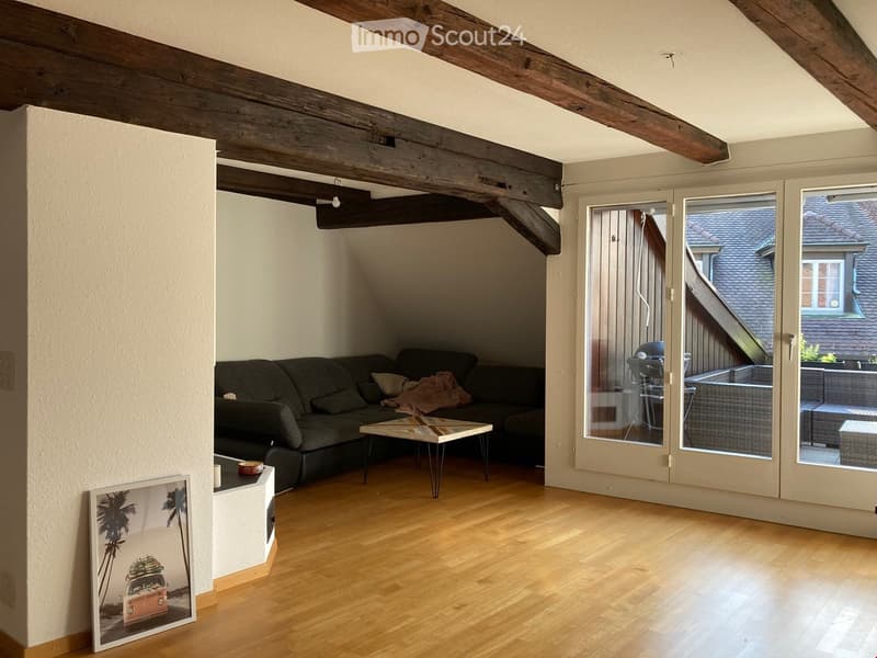 Living room with wooden floor, exposed wooden beams, large windows, sofa, coffee table, and a picture frame on a side table.
