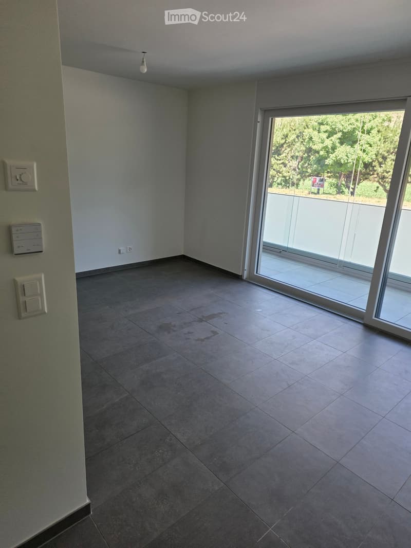 Empty room with tiled floor, white walls, and a large sliding glass door leading to a balcony.