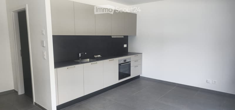 Modern kitchen with white cabinets, black countertops, stainless steel sink, and built-in oven. The space is clean and well-lit with grey tiled flooring.