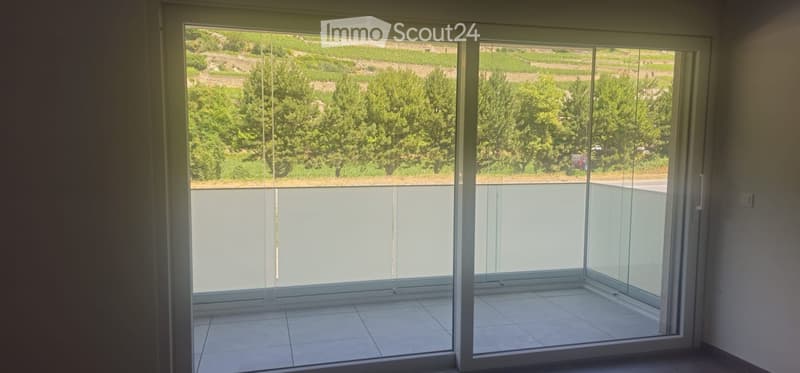 Sliding glass doors open to a tiled balcony with a scenic view of greenery and hills.