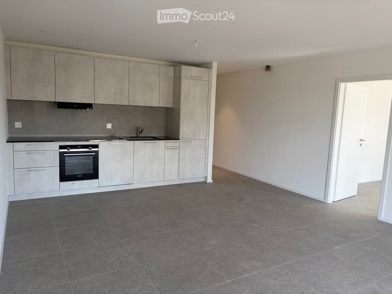 Modern kitchen with grey tiled floor, grey cabinets, and stainless steel appliances including an oven and sink.