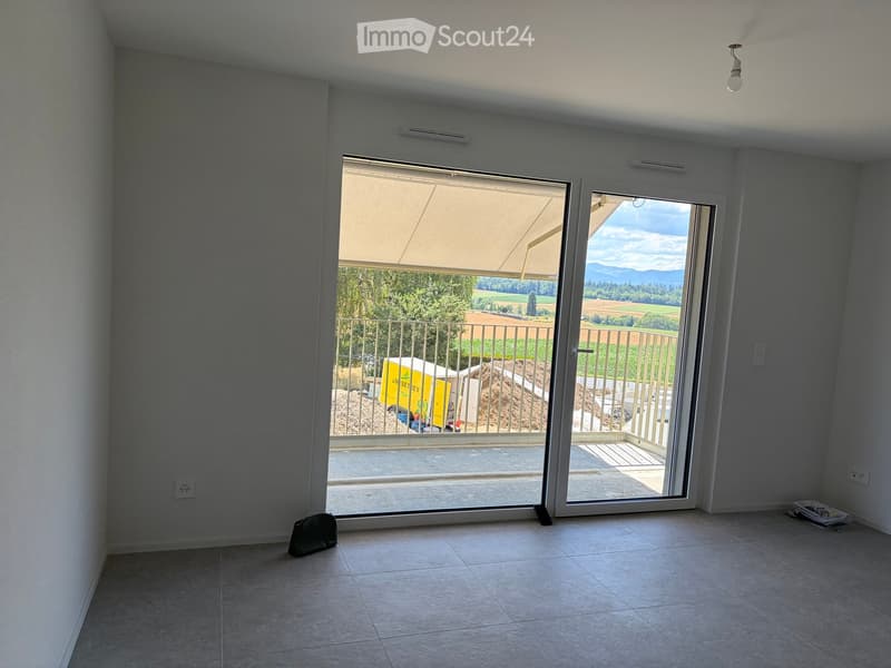 Empty room with tiled floor, large sliding glass doors leading to a balcony with a view of a rural landscape.