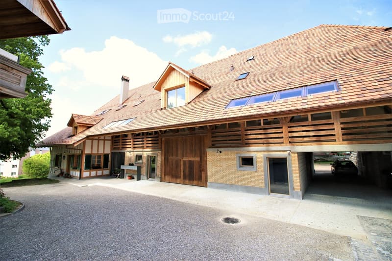 Two-story house with a tiled roof, wooden balcony, garage, and driveway.