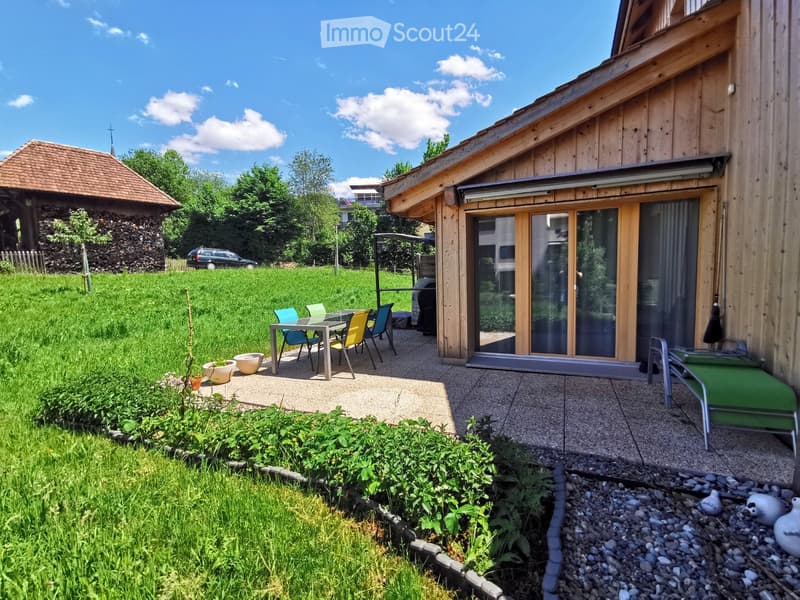 Garden area with a patio, outdoor furniture, and a view of a grassy field and trees.