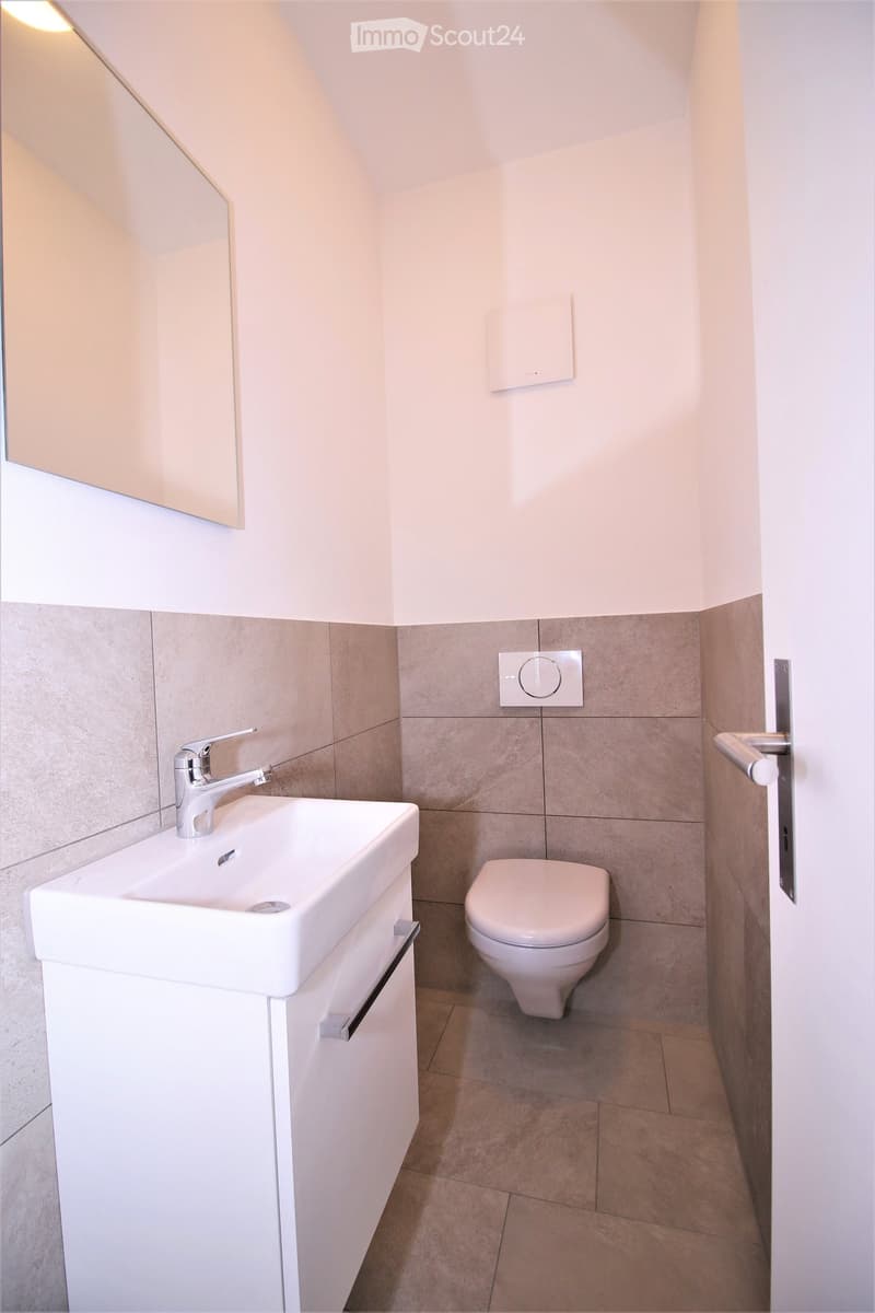 Modern bathroom with a white sink, chrome faucet, and toilet. Light-colored tiles and a sleek design.