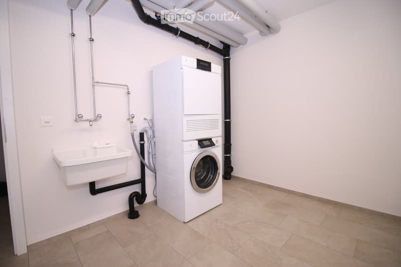A clean, modern laundry room with a white washing machine, a sink, and tiled flooring.