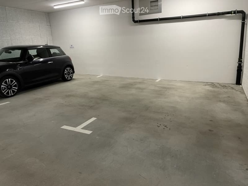 Underground parking space with a single parked car, marked parking spot, and white walls.