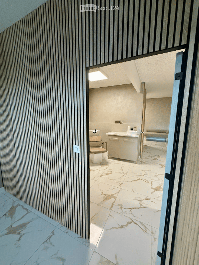 Modern bathroom with marble flooring, white cabinets, a toilet, a sink, and a small stool. The walls are light-colored with vertical wood paneling on one side.