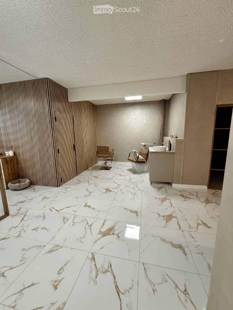 Modern, minimalist room with white marble flooring, wooden panel wall, and a sleek sink area. Two chairs and a stool are positioned in the center.