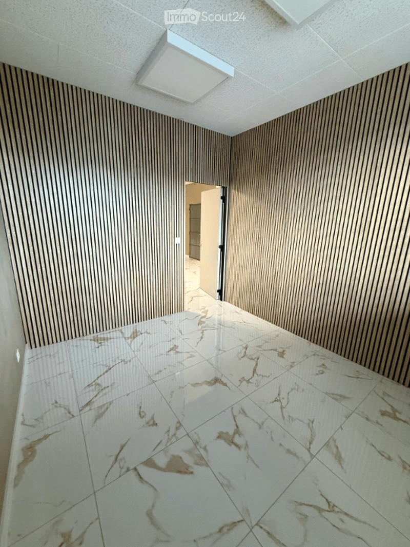 Empty hallway with marble flooring and wood-paneled walls, featuring a white ceiling light fixture and an open doorway leading to another room.